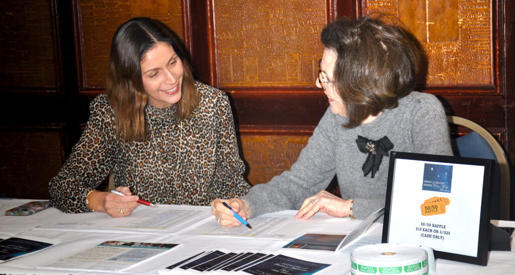 two women sitting at a table looking at one another while reviewing paperwork