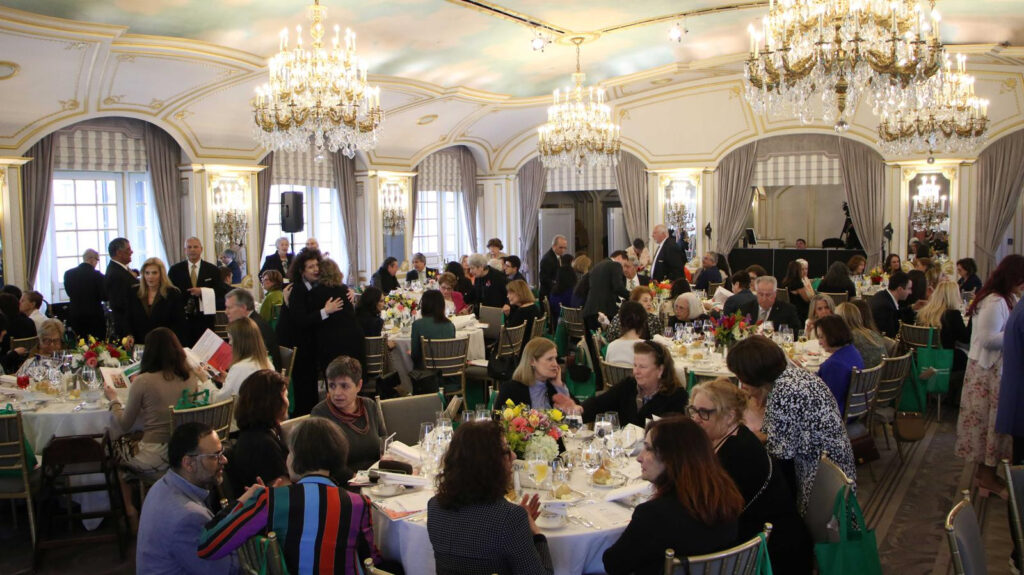 People attending the Gala: a panoramic view of the dining room with attendees seated at their tables or standing and talking to each other